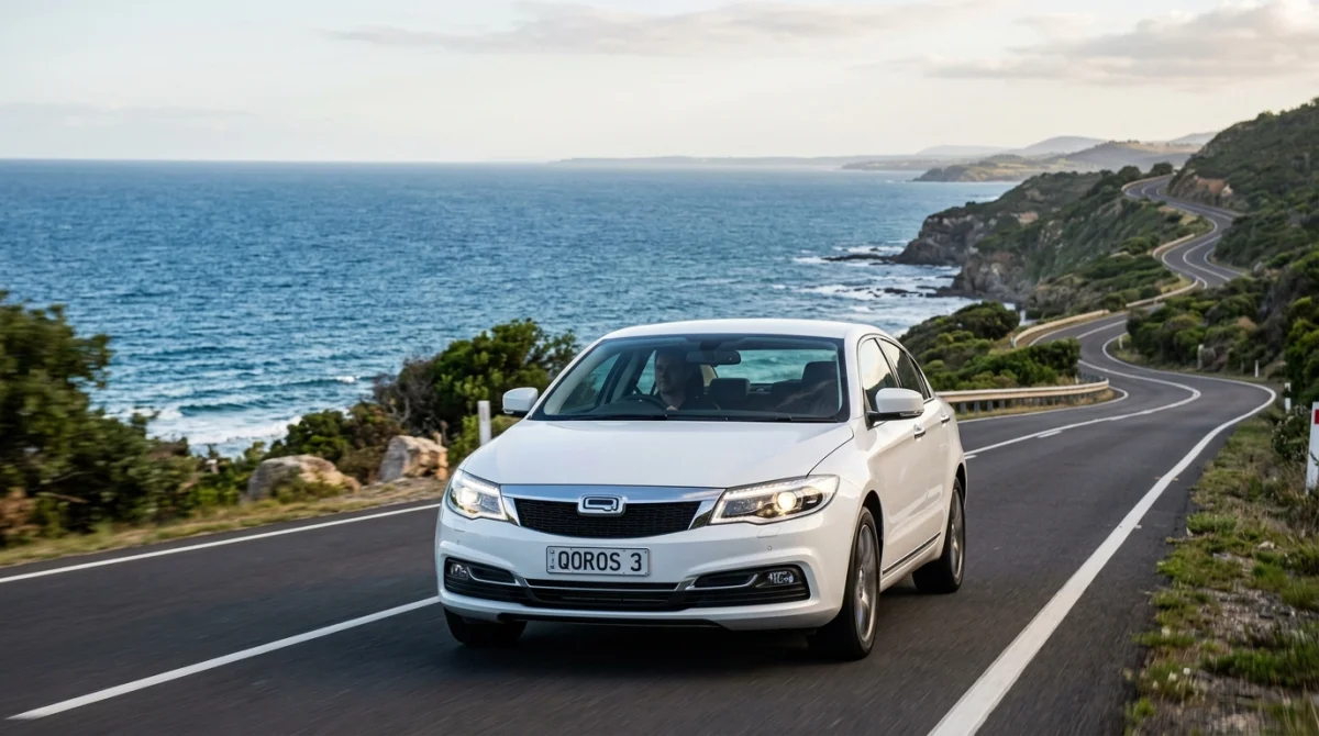 Berline moderne Qoros élégante stationnée sur une route côtière avec vue sur l'océan au coucher du soleil.