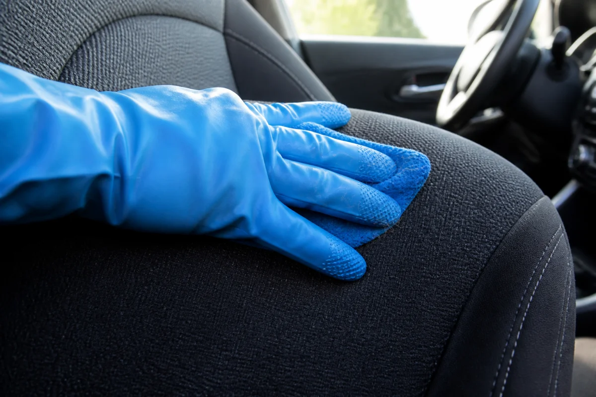 Main gantée de bleu retirant efficacement des poils de chien sur un siège de voiture propre.