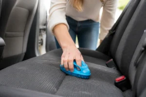 Utilisation d'une brosse en caoutchouc bleu pour enlever efficacement les poils de chien sur un siège de voiture.