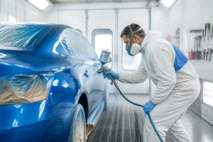 Professionnel d’Atelier Sport Collector appliquant une peinture neuve sur une carrosserie automobile en cabine spécialisée